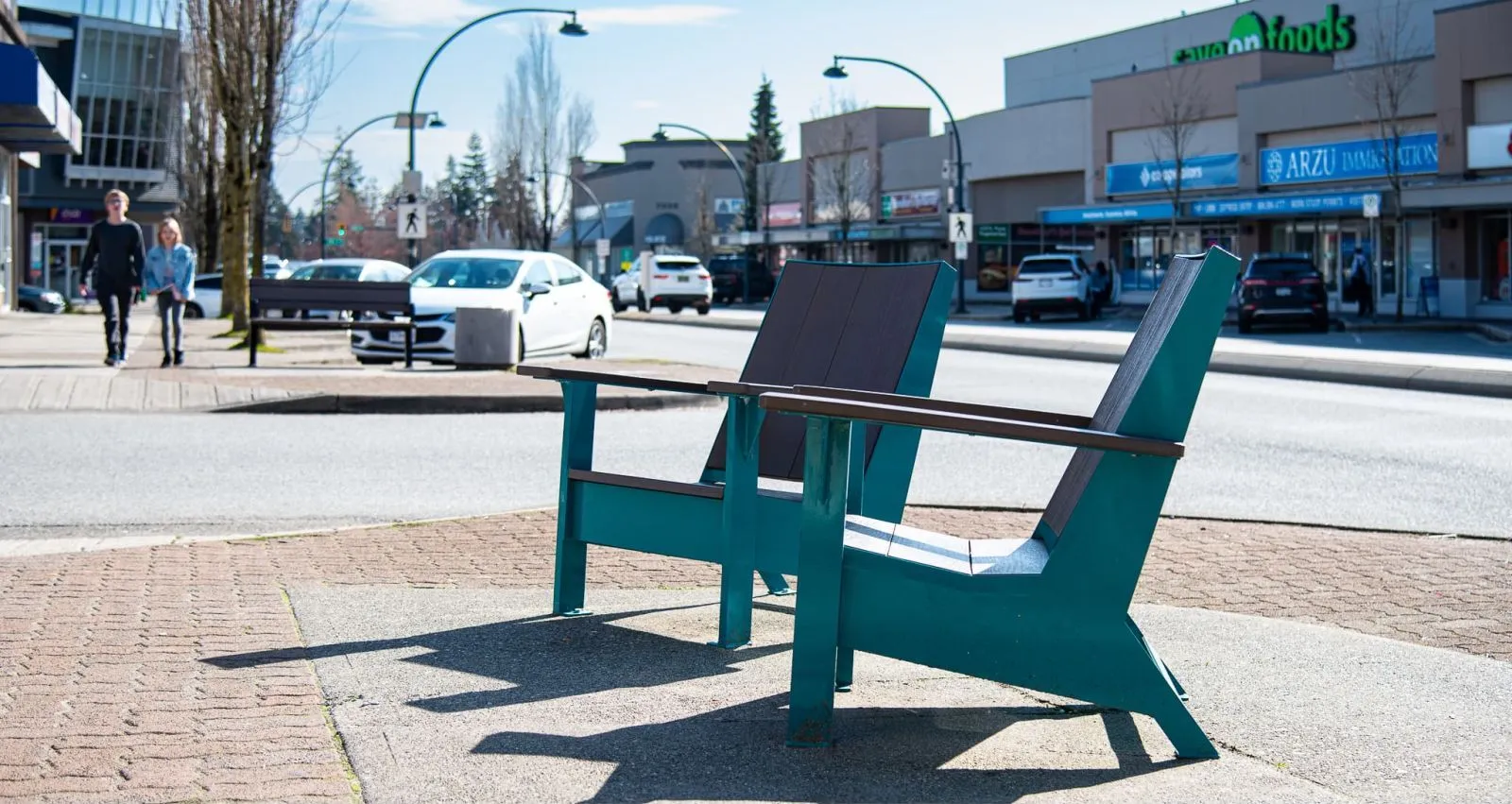 Two Adirondack-style lounge chairs provide seating in a commercial area. The chairs feature teal frames and dark brown recycled plastic lumber.