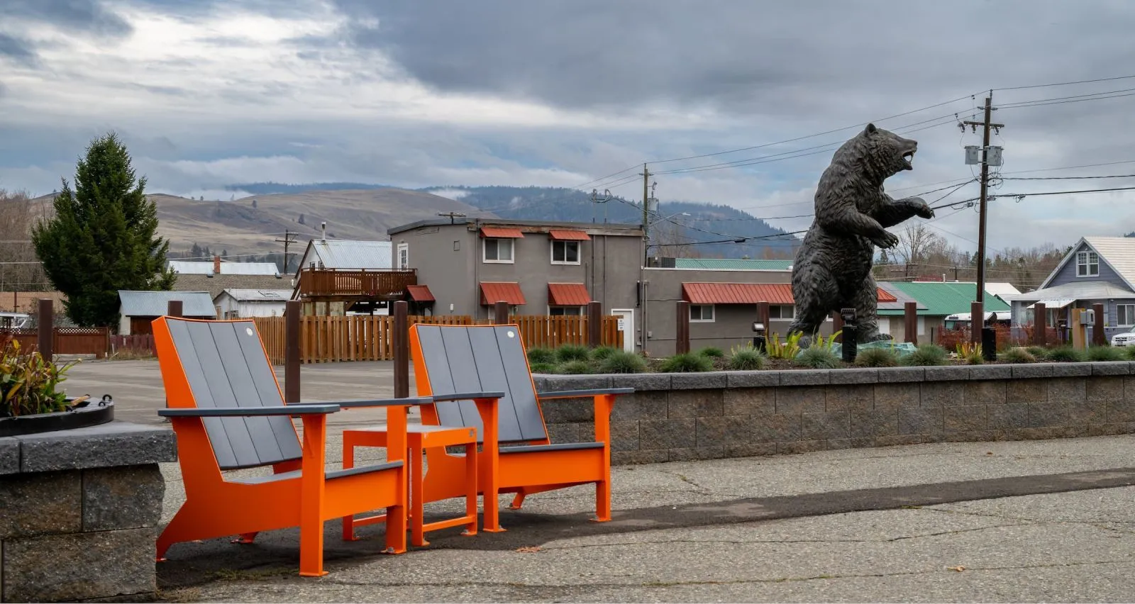 Two lounge chairs and a side table create a relaxing outdoor seating area. The furniture features a vibrant orange frame and gray recycled plastic lumber.
