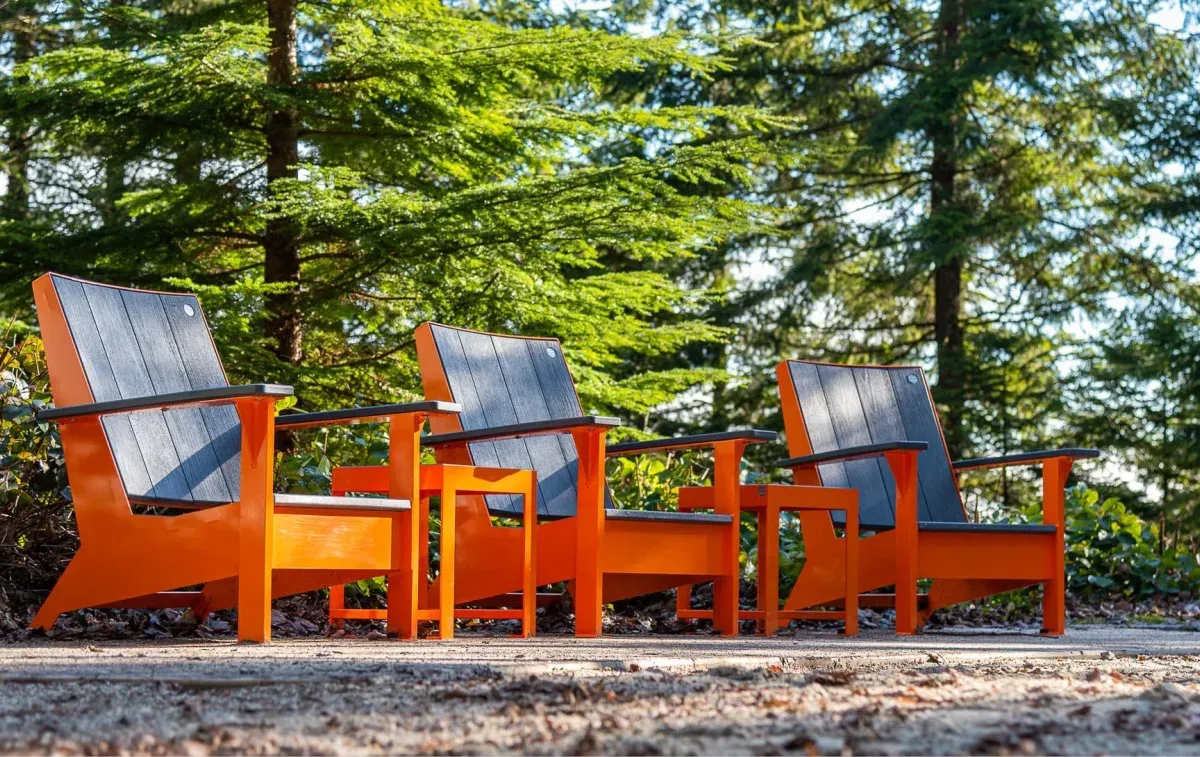 Three lounge chairs provide comfortable outdoor seating in a park setting. The chairs feature recycled plastic lumber seats and backs with powder-coated metal frames.