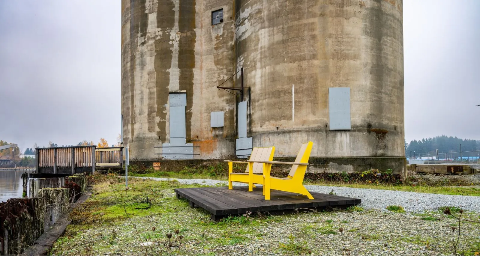 Two lounge chairs sit on a wooden platform in front of a concrete silo. These outdoor chairs provide a comfortable place to relax and enjoy the waterfront view.