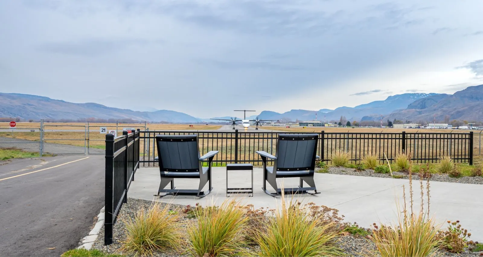 Two JEM Rocking Chairs and a JEM Side Table offer a relaxing spot to watch planes at the May She Soar Memorial viewing area at the Kamloops Airport. The furniture features recycled plastic lumber and powder-coated metal frames.