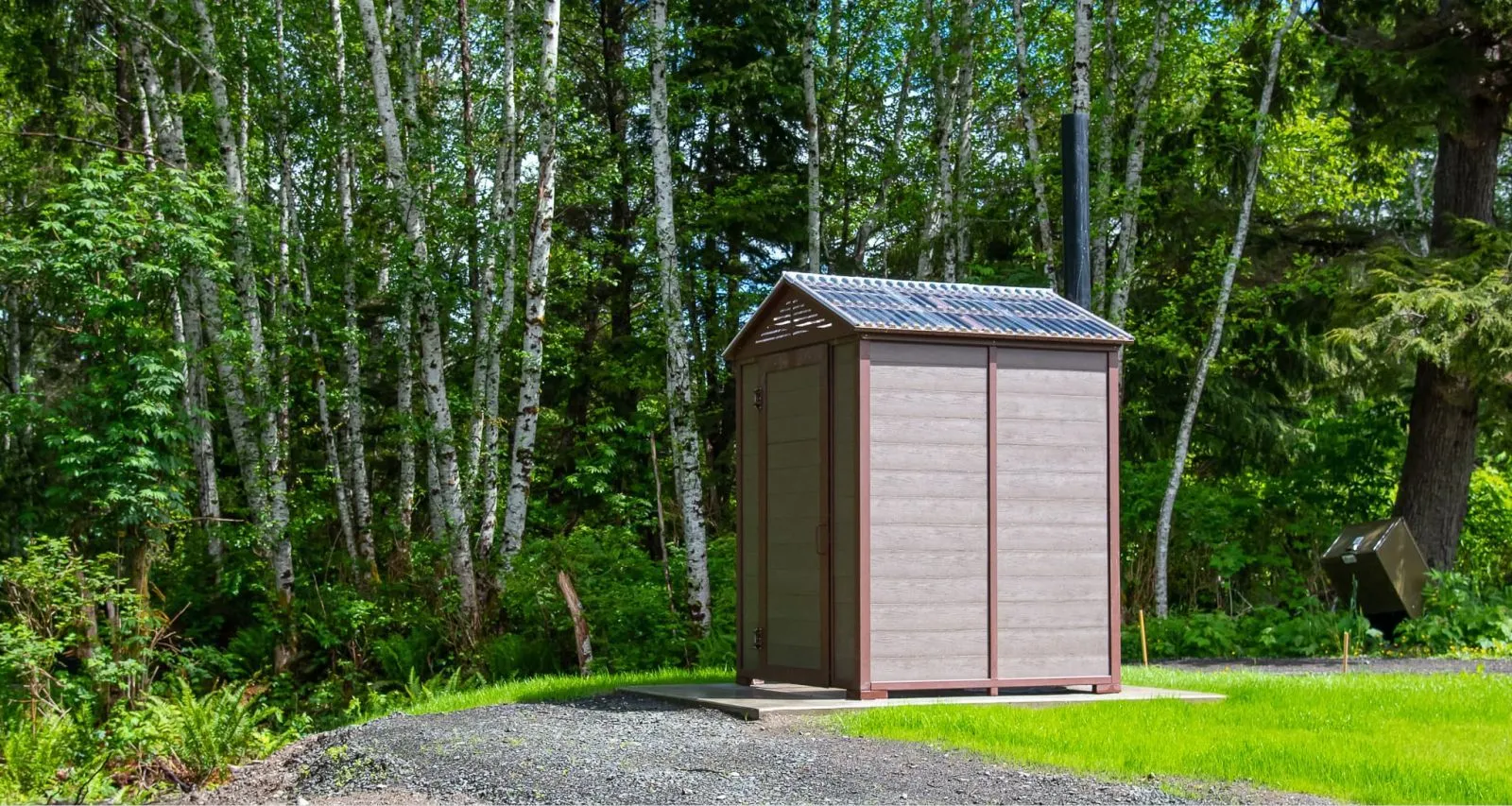 A jumbo outhouse building stands in a wooded area. The structure features recycled plastic lumber and a metal frame.