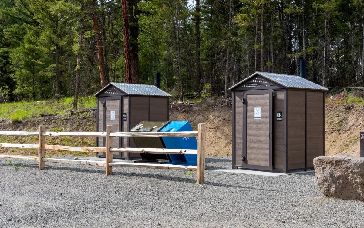 Durable and accessible outhouse buildings are located in a wooded area. These structures provide essential facilities for visitors in outdoor settings.