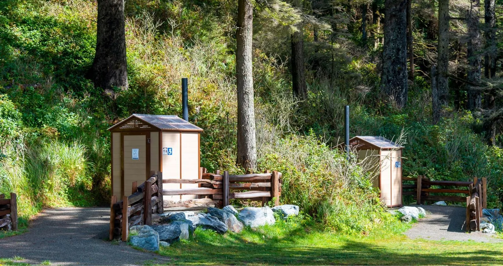 These outhouse buildings provide essential facilities in a natural park setting. The rustic design complements the surrounding forest environment.