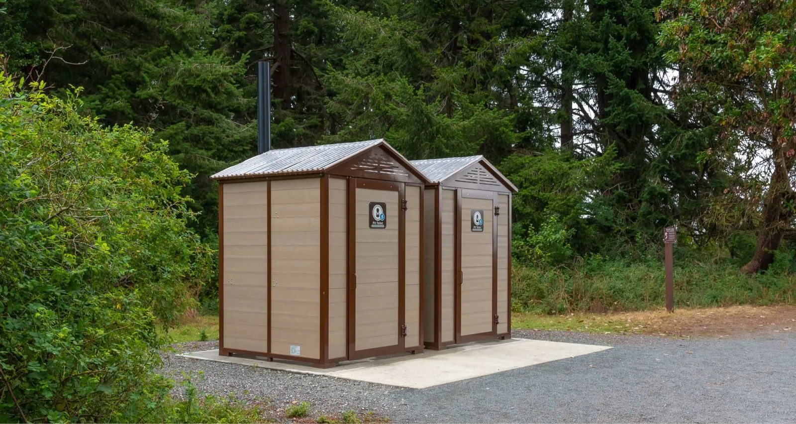These John Jumbo Outhouses provide essential facilities in a natural park setting. The durable construction and simple design blend seamlessly with the surrounding environment.