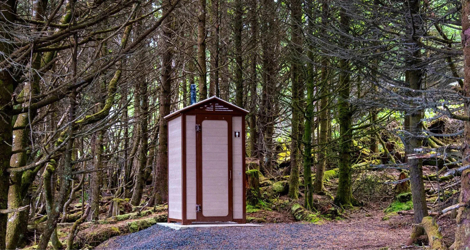 Single outhouse building in a forest setting. The structure features sand-colored recycled plastic lumber and rideau brown trim.