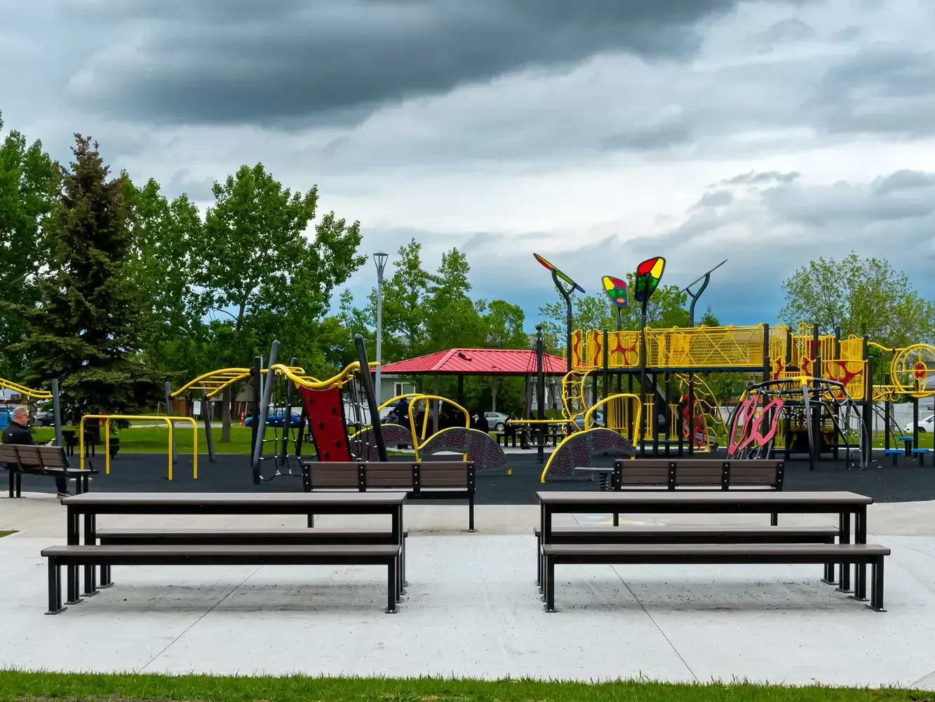 Larson picnic tables and benches provide seating at a playground. The tables feature recycled plastic lumber and black powder-coated frames.