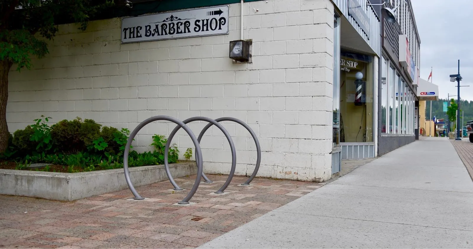 Circular bike racks provide convenient parking outside a barber shop. The racks are installed on a brick-paved area next to a concrete planter.
