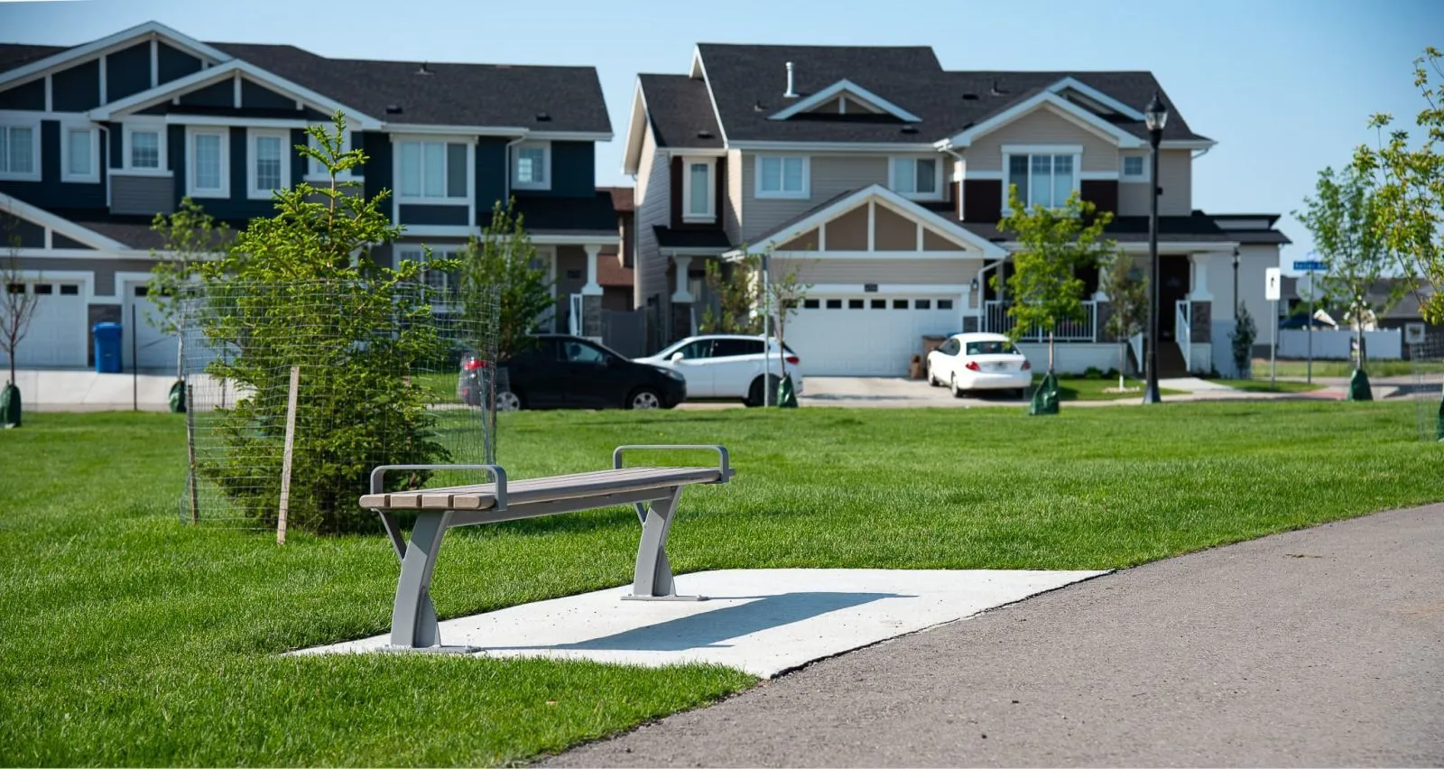 A Parker Backless Bench provides seating in a grassy area of Horizon Station Park. The bench features a simple design with light-colored recycled plastic lumber and a gray powder-coated frame.