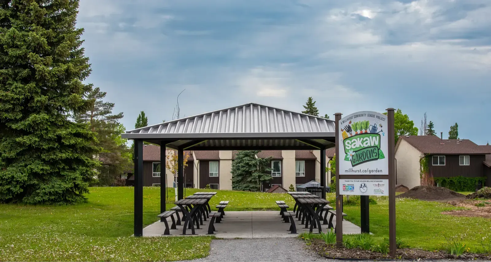 Several Parker Picnic Tables are arranged under a metal shelter in Sakaw Gardens. This outdoor space in Edmonton, Alberta, provides a communal area for residents and visitors.