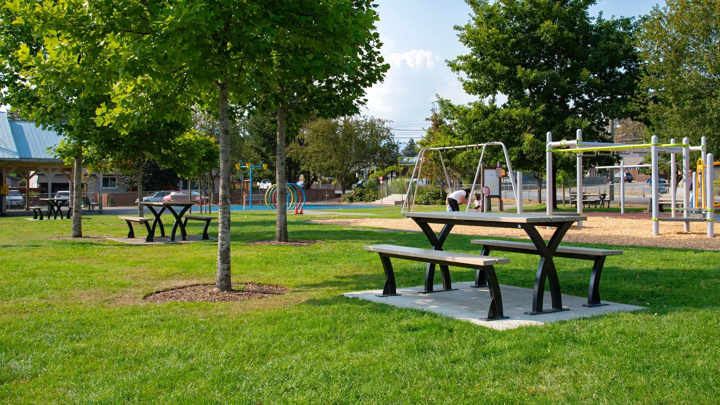 Durable picnic tables with powder-coated frames and recycled plastic lumber tops are installed in a grassy park setting. These tables provide a comfortable space for outdoor gatherings and relaxation.