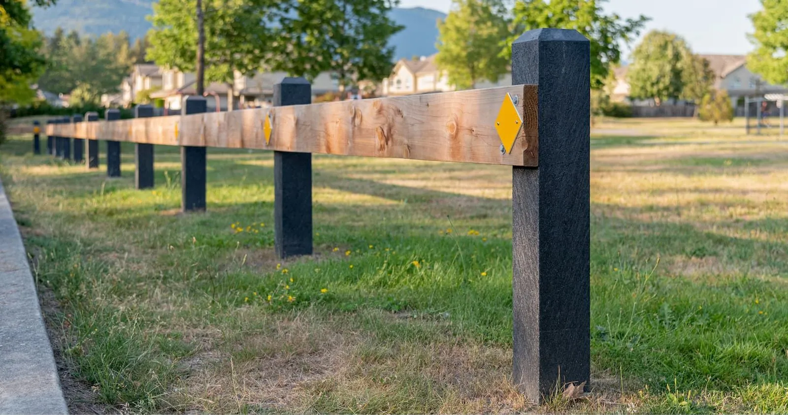 Perma-Post site furnishings create a barrier along a grassy area. The posts feature black recycled plastic lumber and a natural wood rail with yellow reflectors.