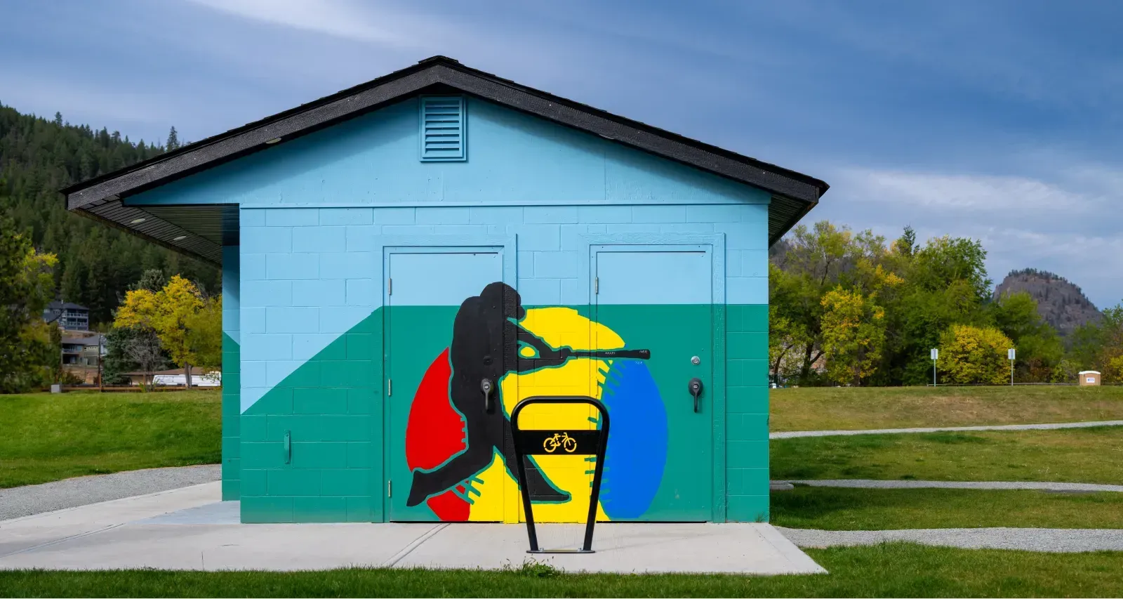 Pipeline two-space bike rack in a park setting. The bike rack is black and stands in front of a colorful building mural.