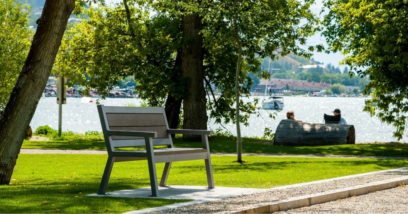 A Rutherford Angled Leg Bench provides seating at Lakeshore Park in Vernon, British Columbia. The bench offers a place to relax and enjoy the view of the lake and surrounding landscape.