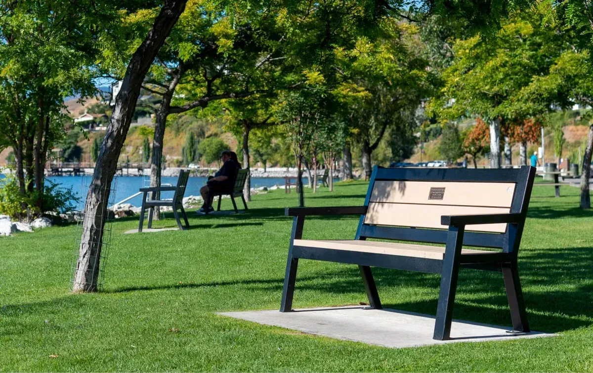 Angled leg memorial bench with recycled plastic lumber seating and black powder-coated frame, installed in a lakeside park setting. This bench provides a comfortable and durable seating option for enjoying the scenic views.