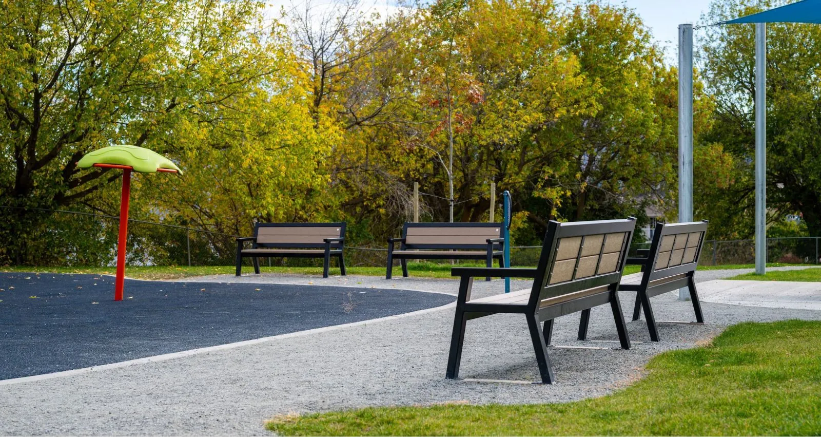 Several benches are installed in a park setting with fall foliage. These benches provide seating for visitors to enjoy the outdoors.