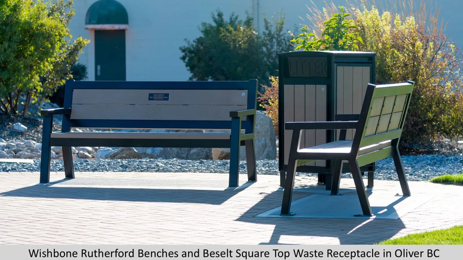 Site furniture including a Rutherford bench and Beselt Square Top waste receptacle are installed in a paved outdoor area. The bench and waste bin are made with recycled plastic lumber and powder-coated metal.