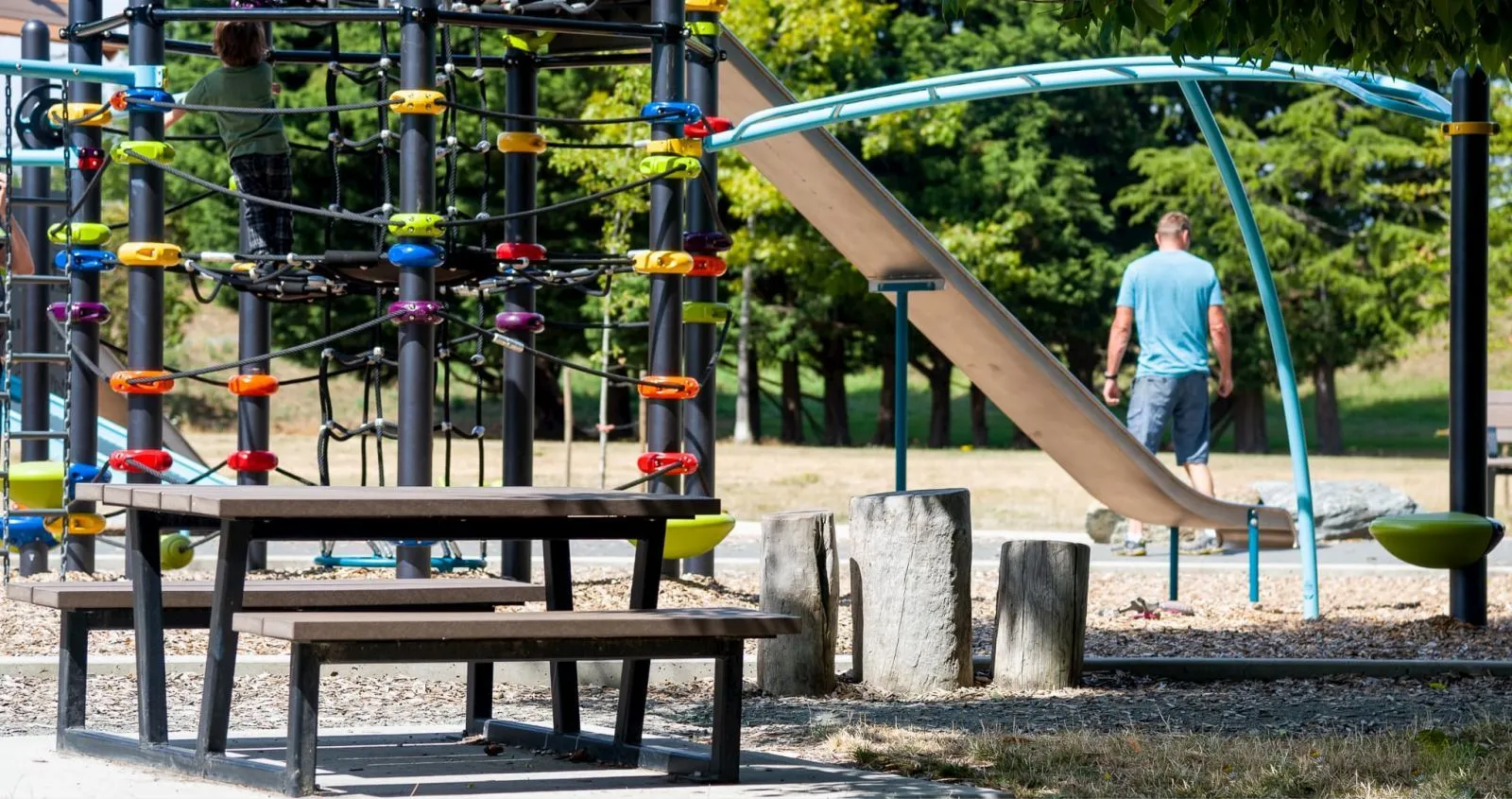 Child-sized picnic table in a playground setting. The table features a dark frame and brown recycled plastic lumber.