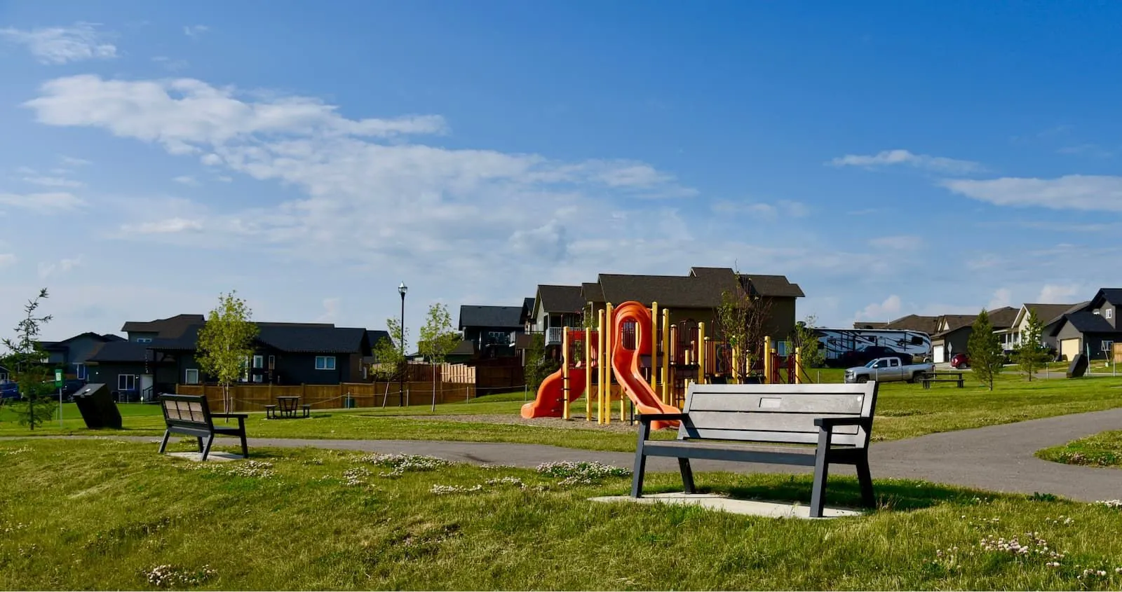 Rutherford benches provide seating in a community park with a playground. These benches feature recycled plastic lumber and a durable powder-coated metal frame.