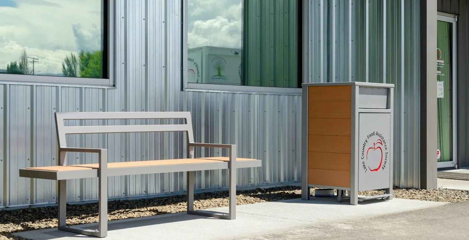 Skyline bench and waste receptacle outside the Lake Country Food Assistance Society. The bench features a metal frame and recycled plastic lumber seat.