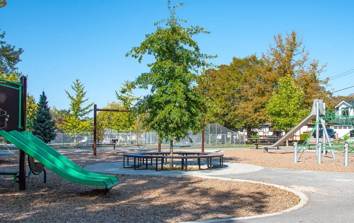 Curved bench encircles a tree in a park setting. The bench provides seating around the tree, enhancing the park's landscape.
