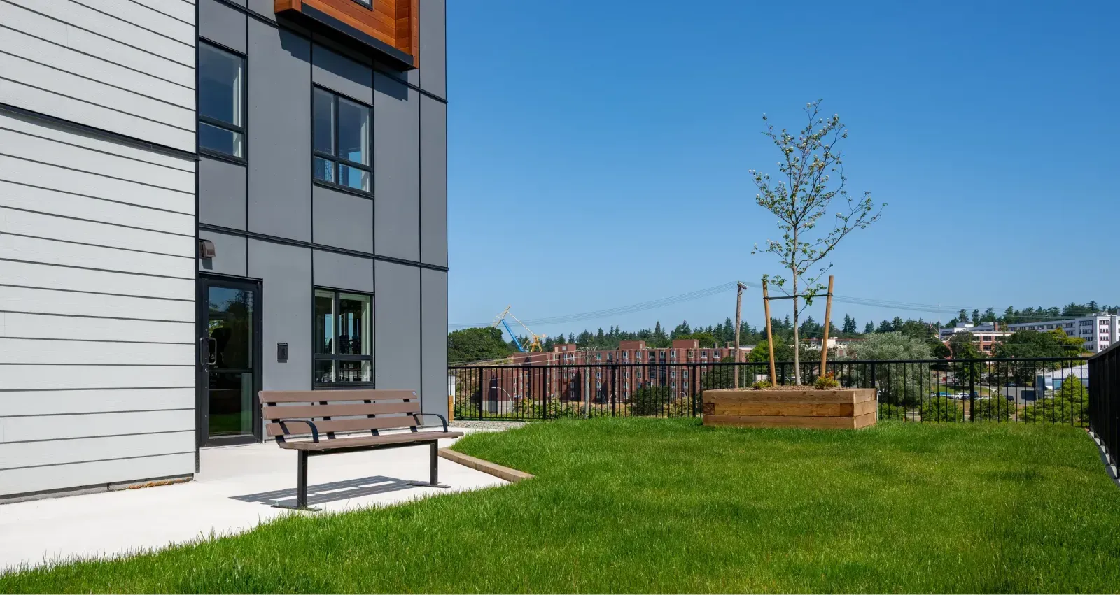 A Standard bench provides seating on a rooftop patio with artificial grass. The bench features brown recycled plastic lumber.