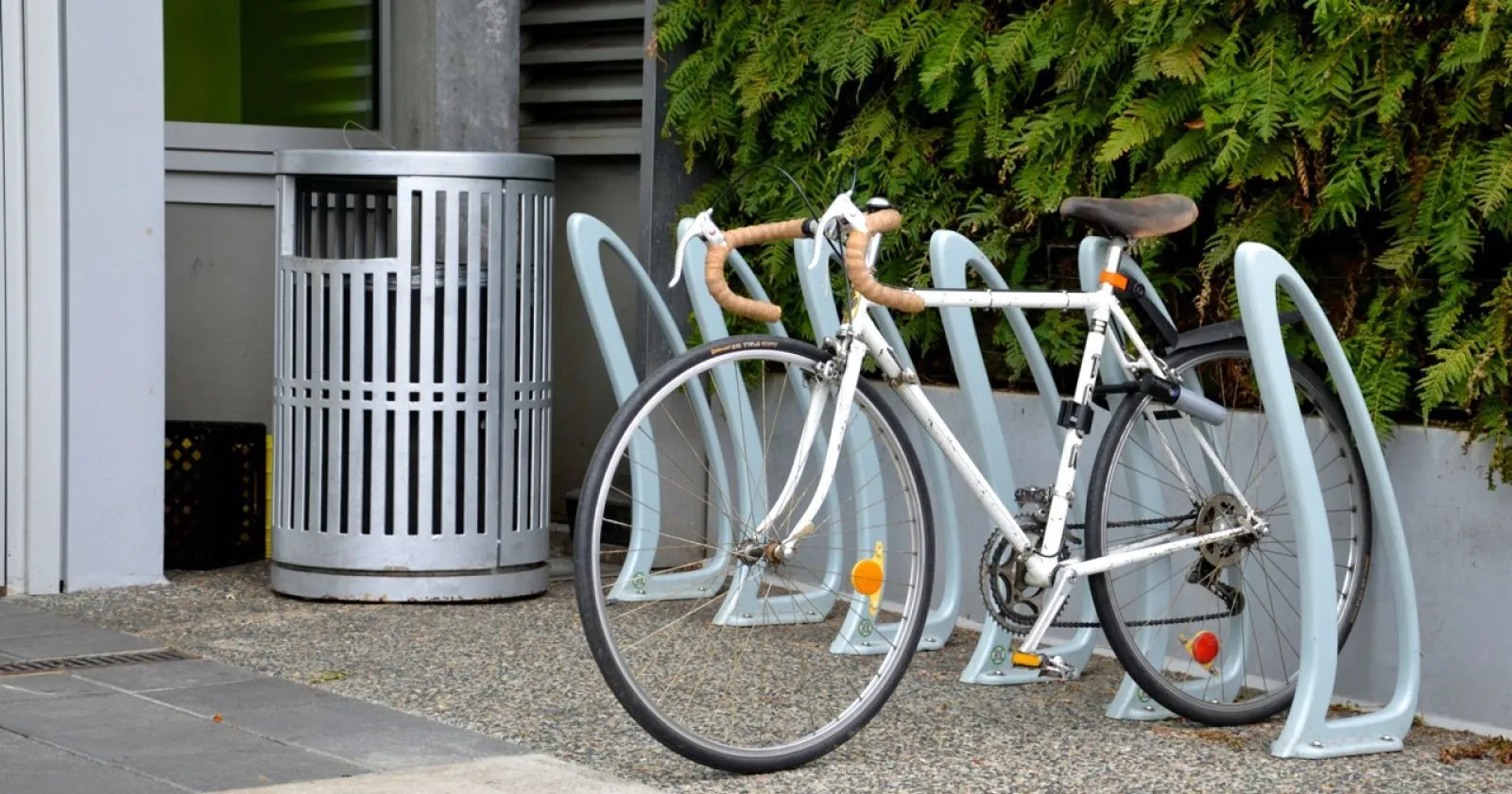 Galvanized steel litter bin and bike rack provide convenient amenities in an outdoor setting. The bike rack is powder coated in a light grey.