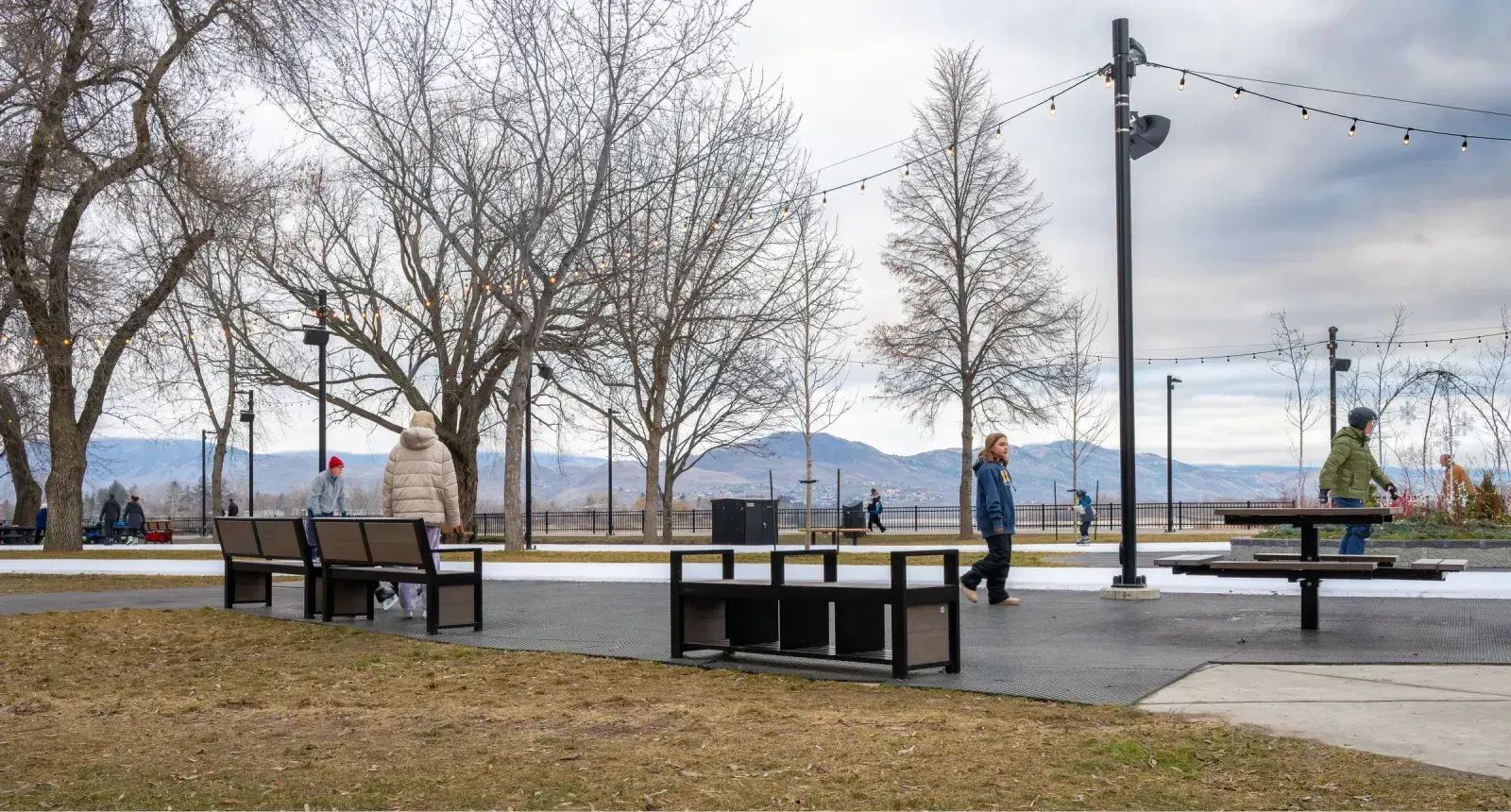 Outdoor benches and a picnic table furnish a park area with a mountain backdrop. The site furniture features recycled plastic lumber and powder-coated metal frames.