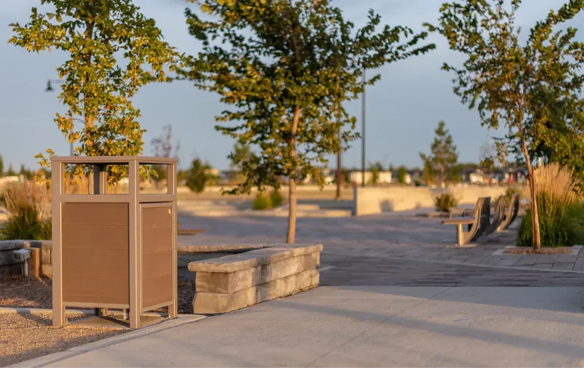 This park features an easy-access waste receptacle with recycled plastic lumber panels and a powder-coated metal frame. The surrounding area includes benches and landscaping.