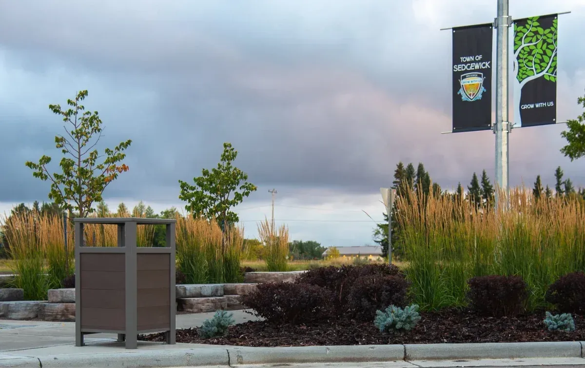 Urban Form Easy Access Waste Receptacle in a landscaped area. The bin features recycled plastic lumber and a powder-coated metal frame.