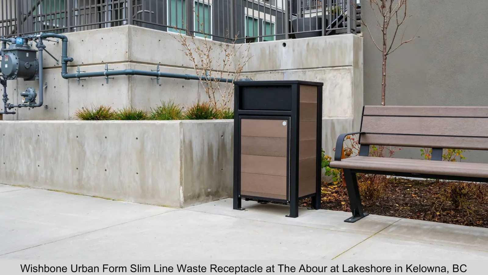 Slim line waste receptacle featuring horizontal recycled plastic lumber slats and a black powder-coated frame. This modern trash bin is located at The Abour at Lakeshore in Kelowna, British Columbia.