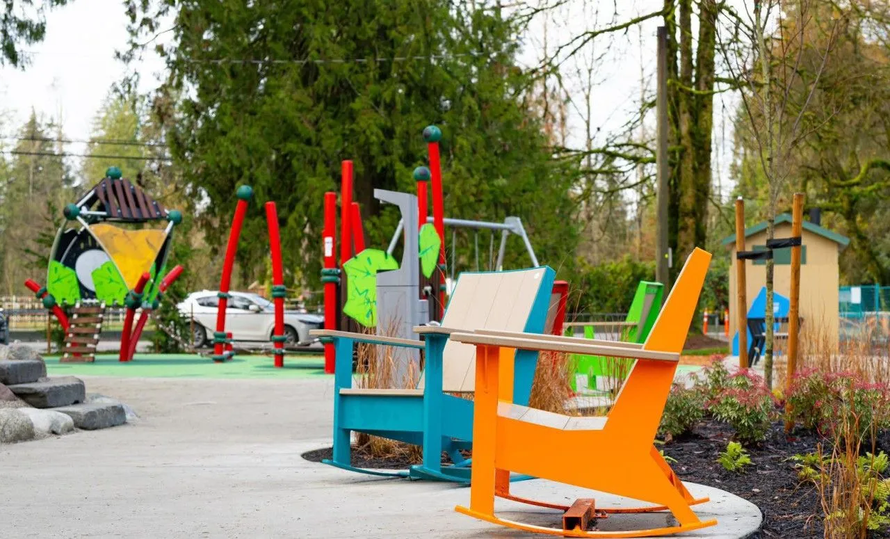Colorful rocking chairs add a playful touch to this park's playground area. These durable chairs provide a comfortable spot for relaxation and socializing in an outdoor setting.