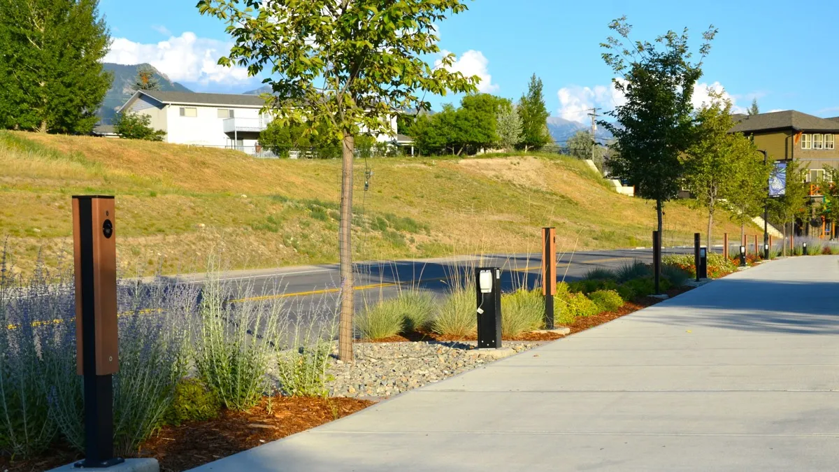 Perma-Post site accents line a walkway, providing a modern and functional element to the landscape. These posts feature a wood-look finish and black accents, complementing the surrounding greenery and architecture.
