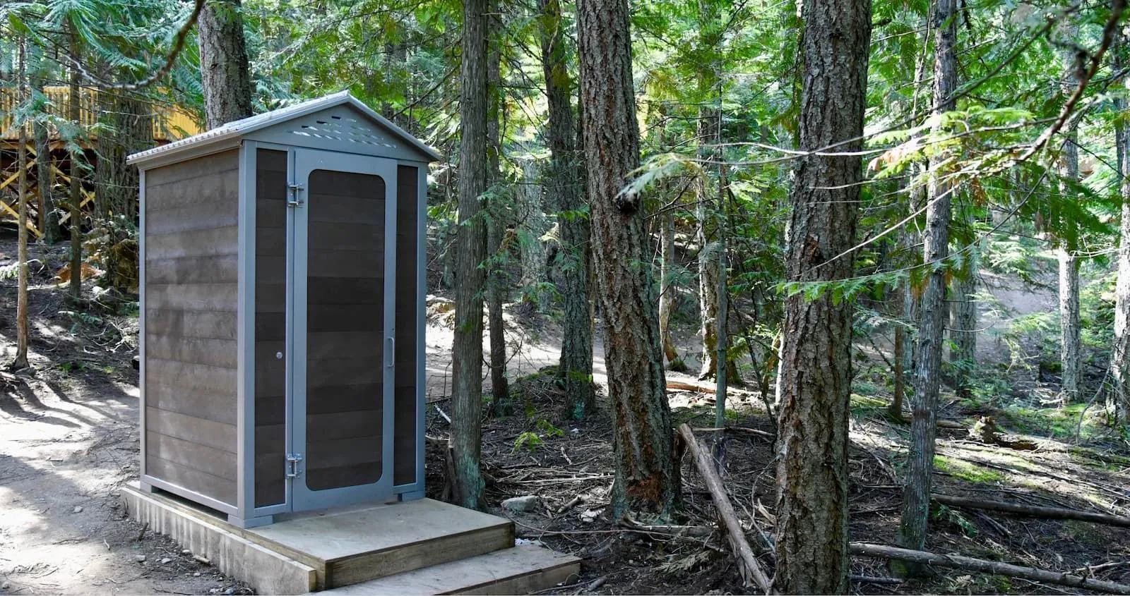 This outhouse building features durable recycled plastic lumber and a powder-coated metal frame. It provides a functional and eco-friendly restroom solution for outdoor settings.