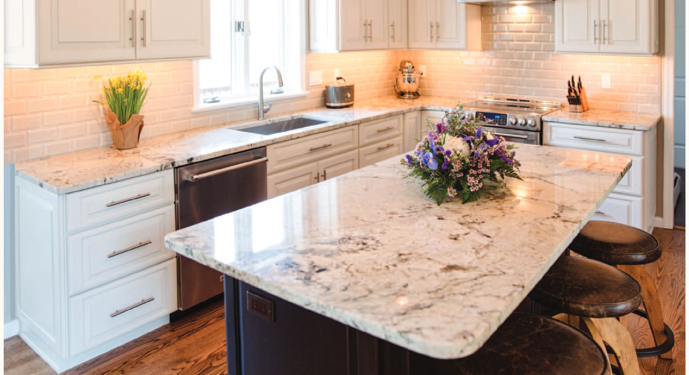 Bright kitchen with white cabinets, granite countertops, and wooden stools.