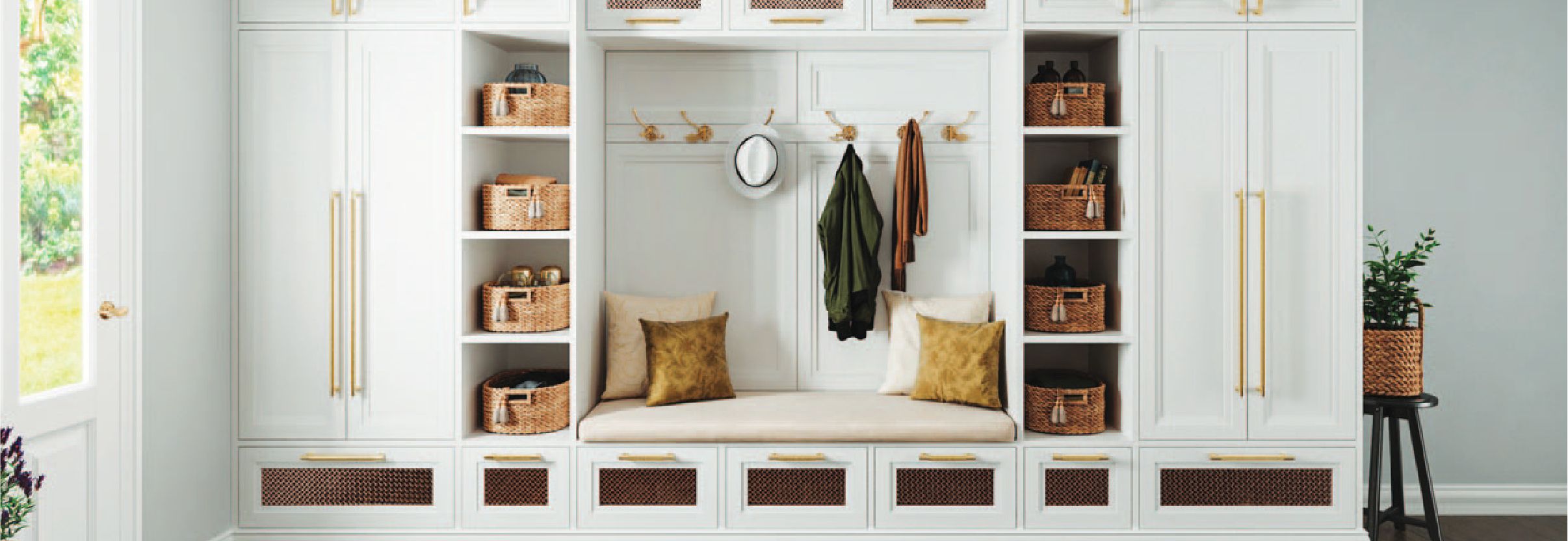 A white built-in shelving and storage unit with a bench, baskets, and hooks, framed with overhead lighting.