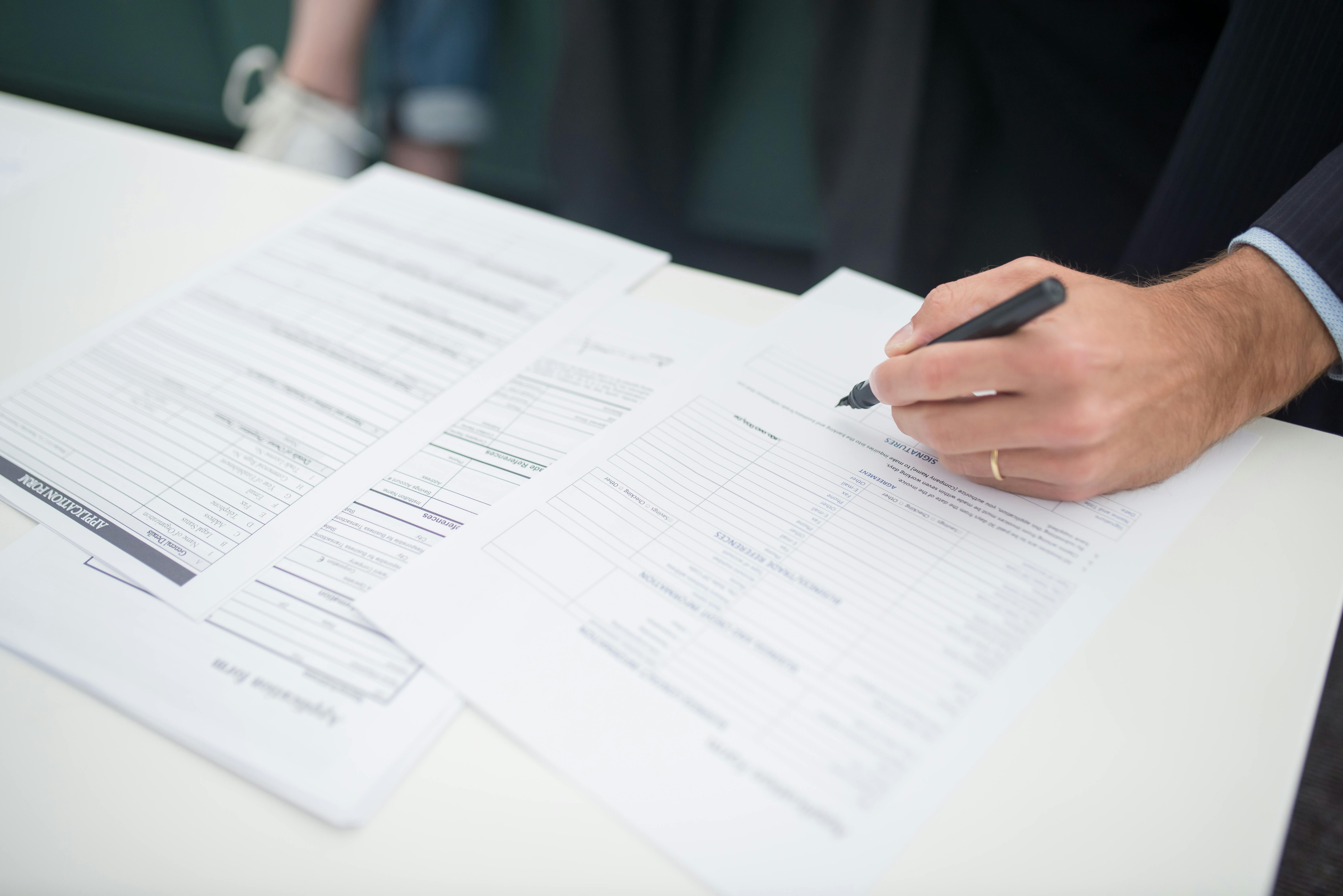 A close-up, photorealistic image of a homeowner's hand holding a pen, about to sign a detailed insurance policy document that sits on a wooden table.