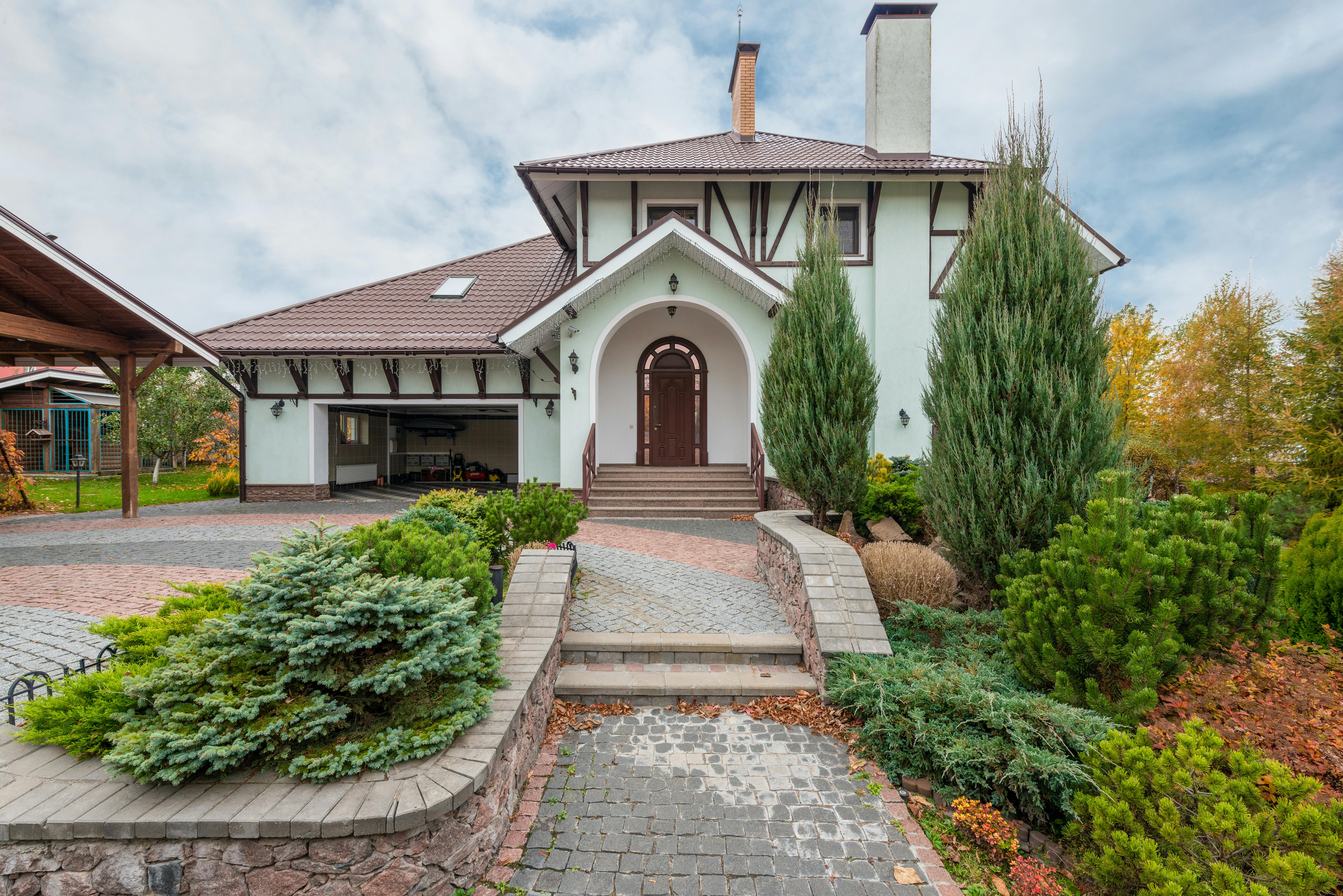 An elegant front porch view of a house with fresh exterior paint and vibrant landscaping including seasonal flowers and shrubs. The scene is complemen