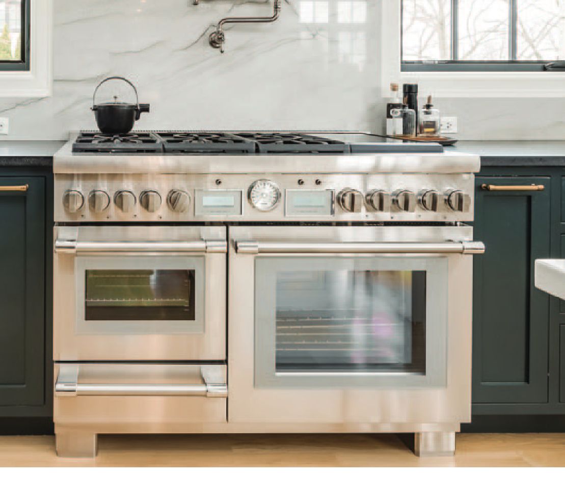 A modern kitchen with a large stainless steel oven, dark cabinets, and a marble backsplash.