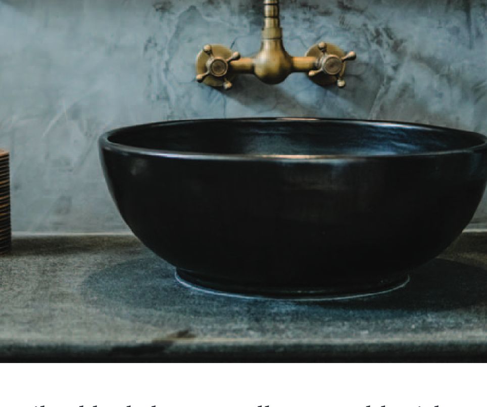 A black vessel sink with a brass faucet against a cement countertop.