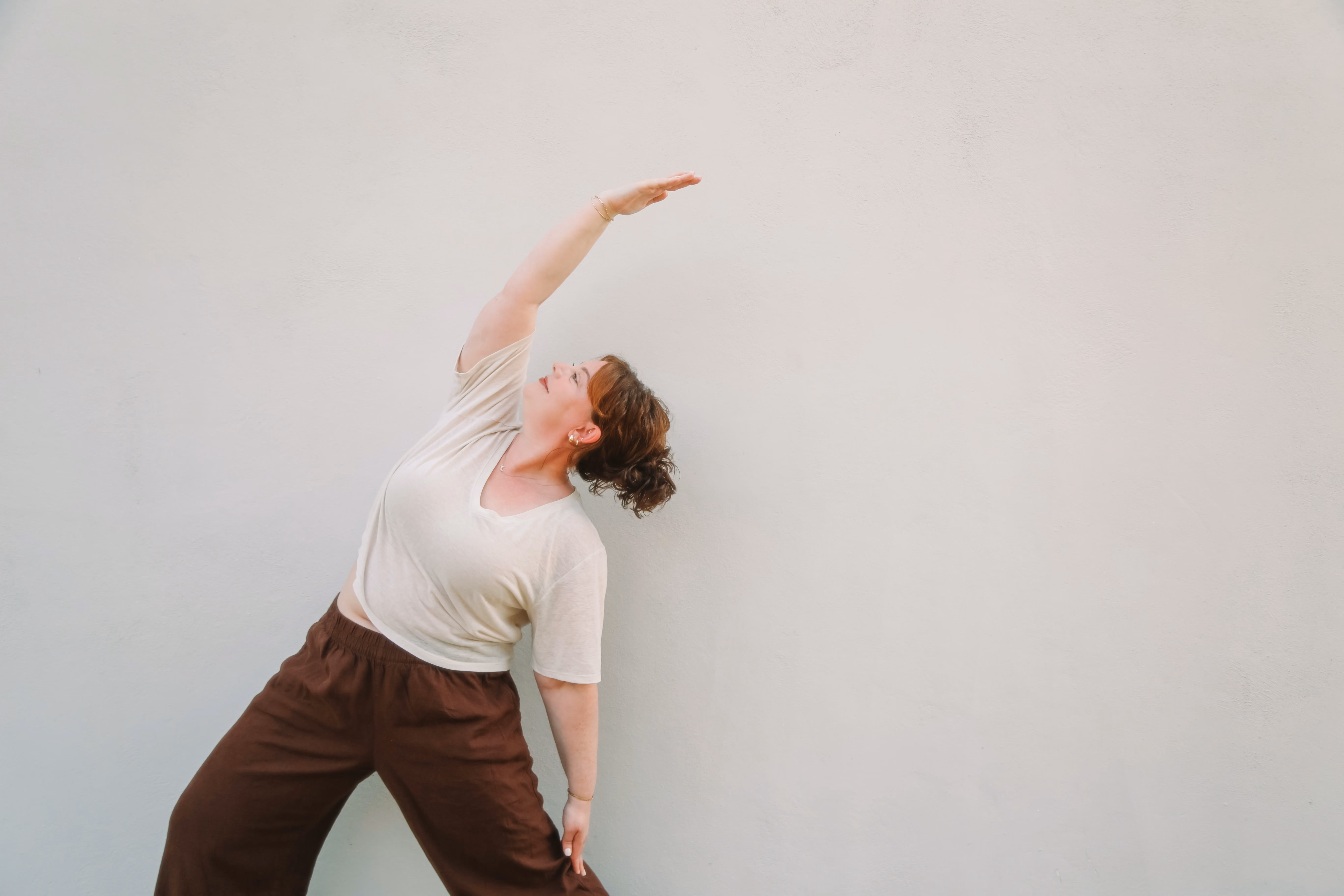 Elise in a side-stretching yoga pose against a white wall