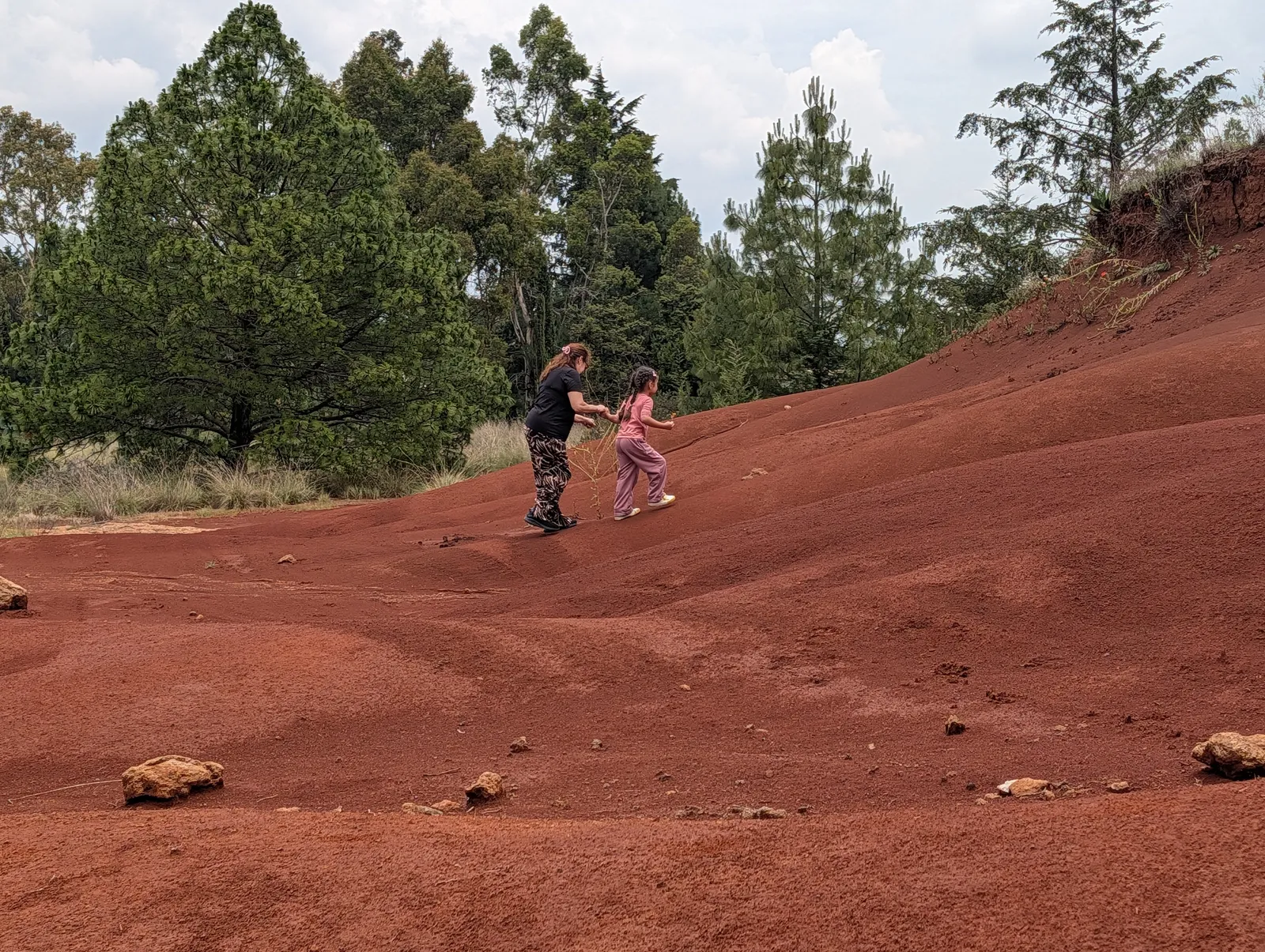 Persona adulta y niña caminando por las Dunas Rojas de Amealco durante una salida de senderismo en Querétaro.