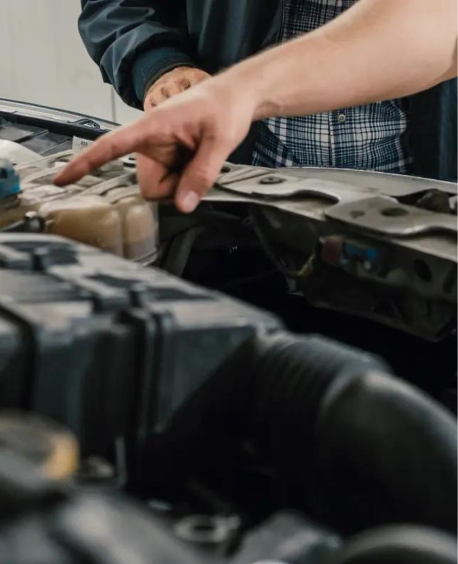 A man pointing to a part inside of the engine compartment of a vehicle