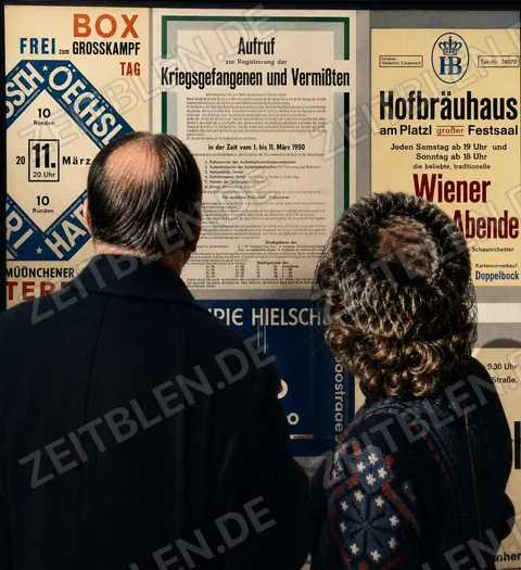 Passanten vor einem Münchner Plakataushang und lesen das Plakat über Kriegsgefangene und Vermisste.