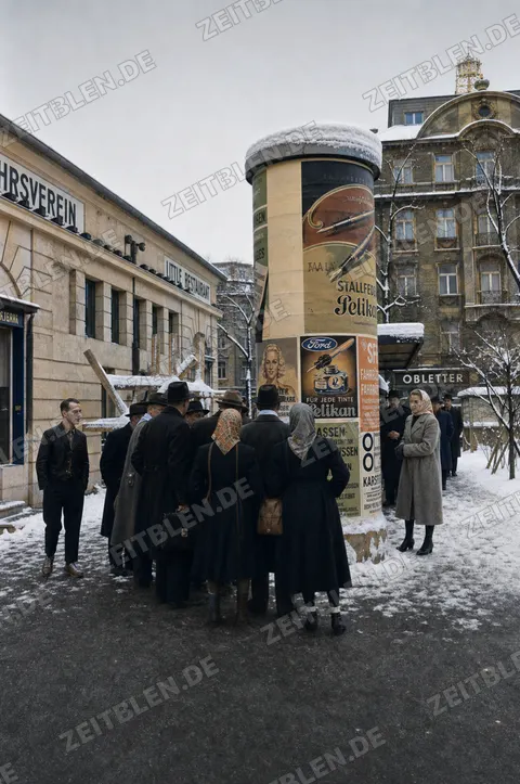 Menschen vor Plakaten an einer Litfaßsäule