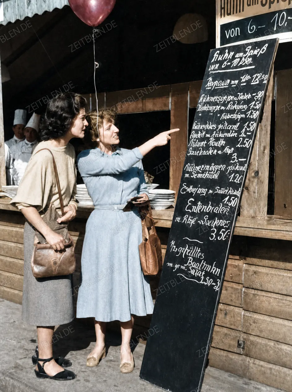 Besucherinnen lesen die Speisekarte an einem Oktoberfest-Stand