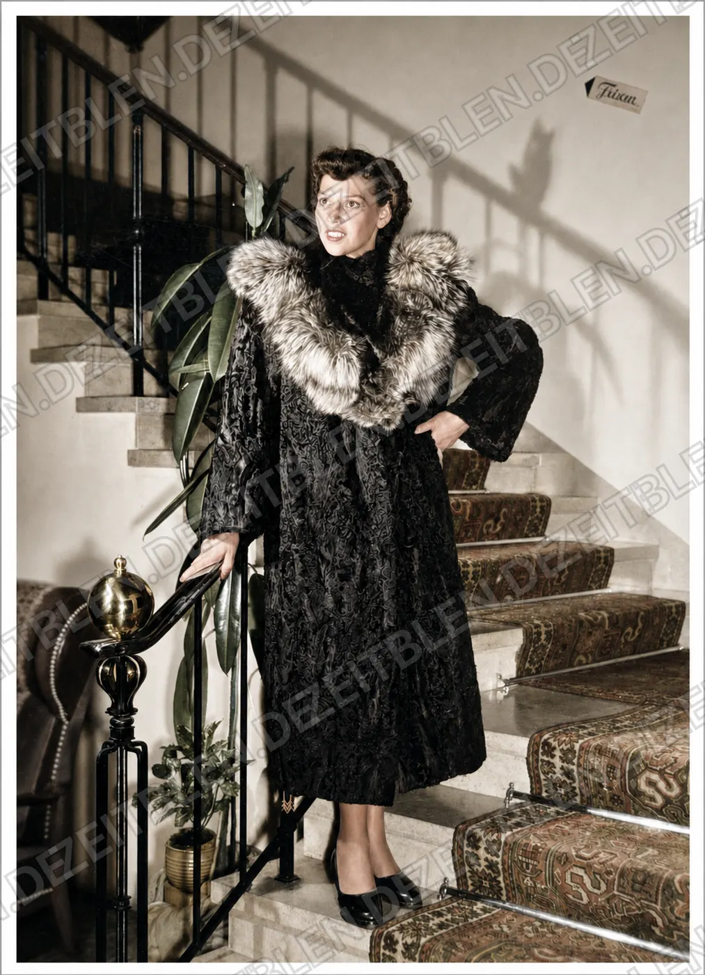 Model mit hellem Pelzkragen auf der Hoteltreppe