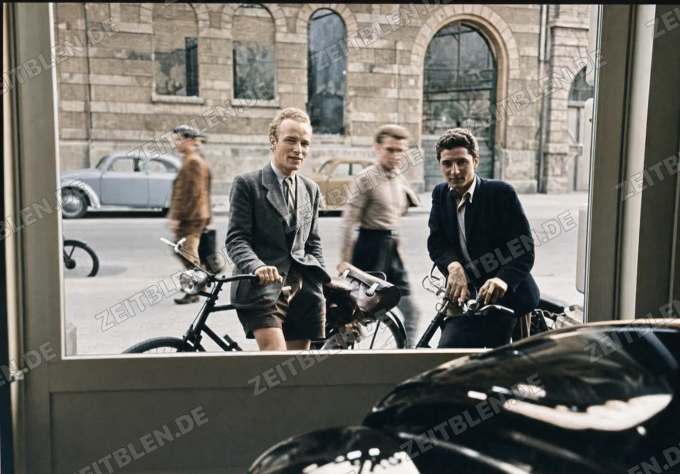 Zwei Radfahrer vor einer Münchner Ladenfront mit Automobil