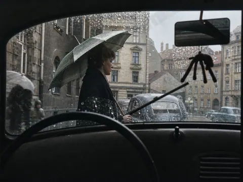 Fußgänger mit Regenschirm vor Fahrzeug, 1956