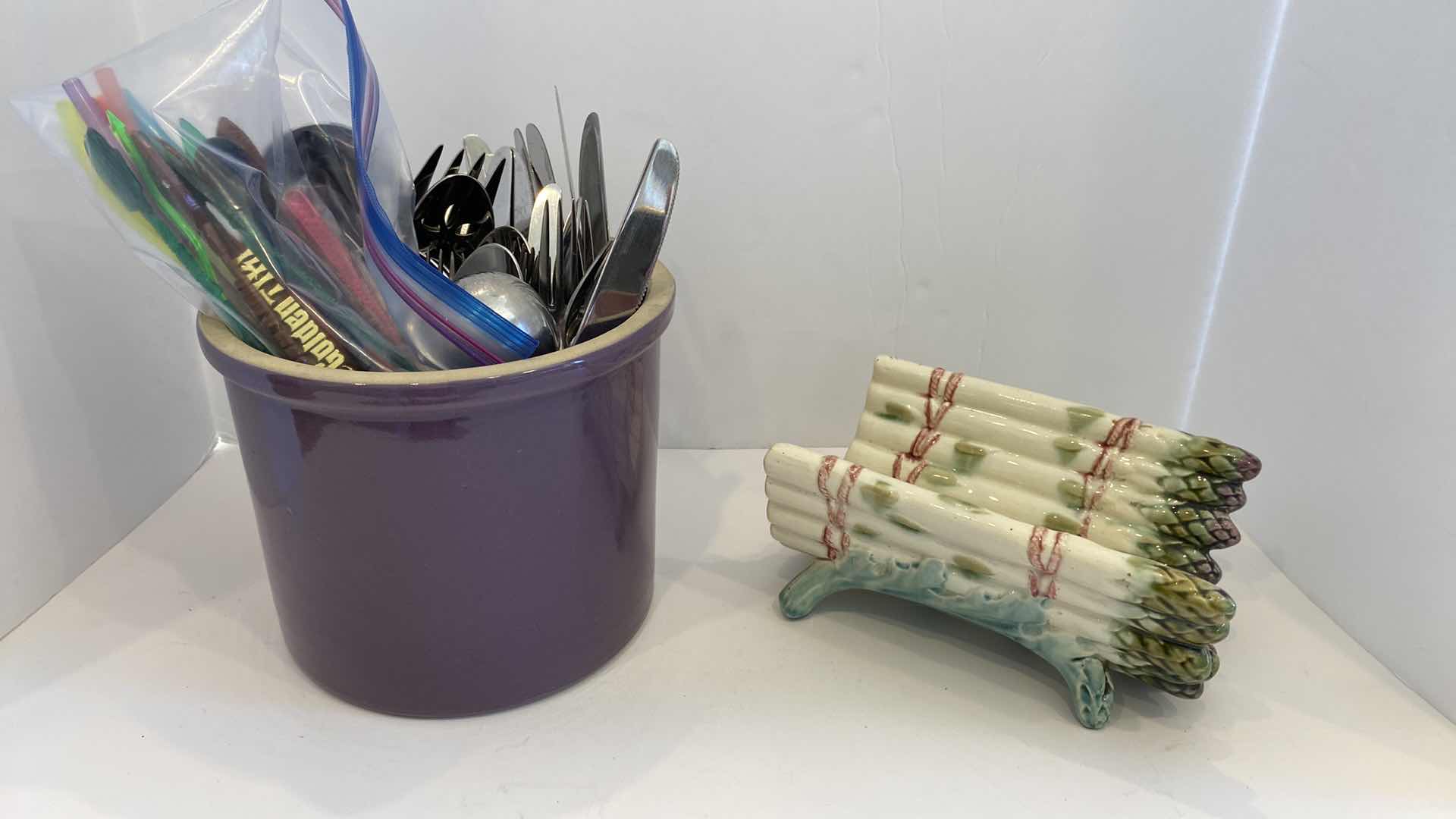 Photo 1 of CONTENTS OF KITCHEN CABINET
 PURPLE CROCK WITH SILVERWARE AND CERAMIC ASPARAGUS DECOR